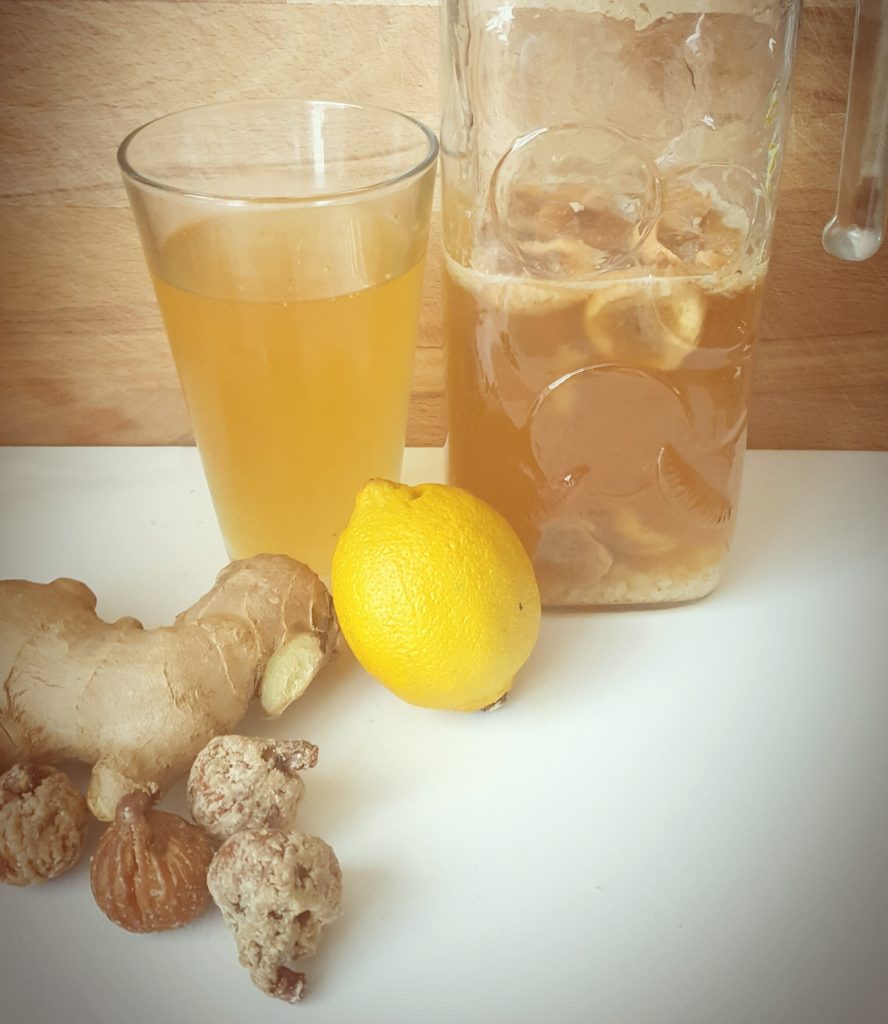 Foto van een kan met waterkefir, citroen, gember en een glas gevuld met gezeefd waterkefir.